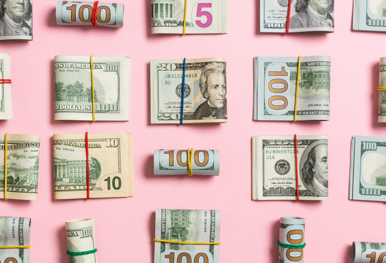 different folded stacks of money on a pink background.